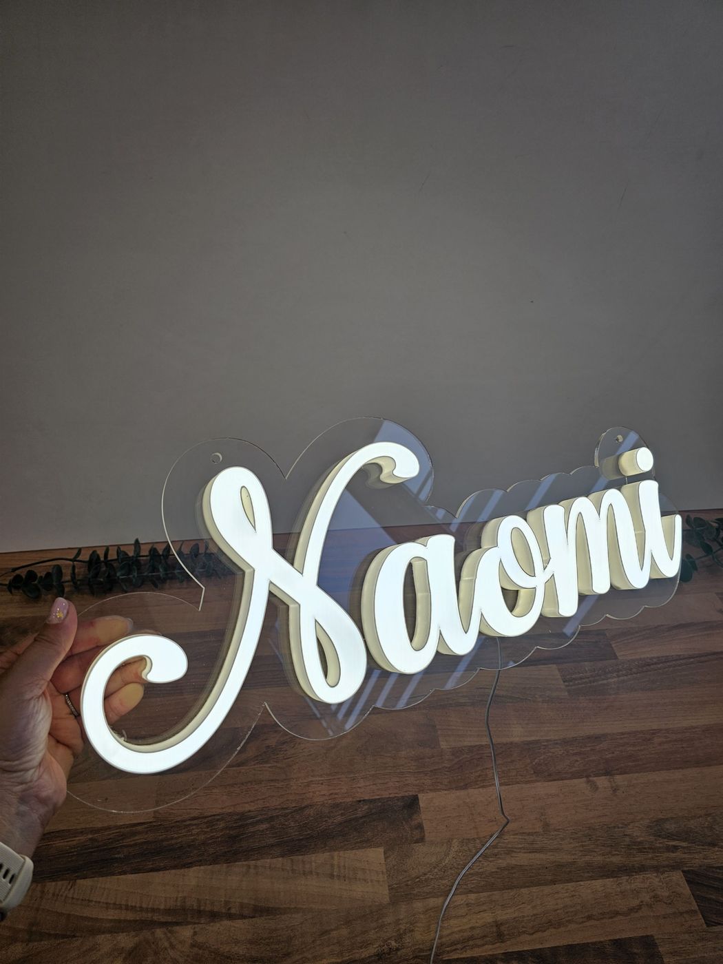 Numele „Naomi” luminos, cu suportul transparent decupat după litere